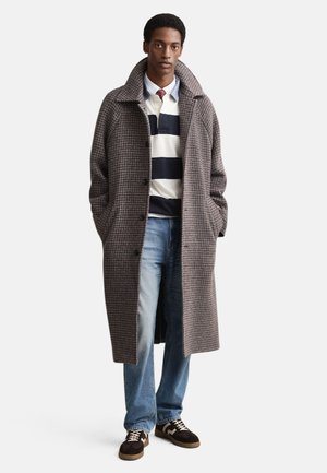 Grauer Hahnentritt-Übermantel mit weitem Kragen, Knopfverschluss und Seitentaschen, getragen über einem navy gestreiften Hemd und blauen Jeans.