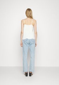 Witte satijnen cami-top met verstelbare bandjes, gecombineerd met lichtblauwe rechtlopende jeans en zwarte block-heeled sandalen. Minimalistisch ontwerp.