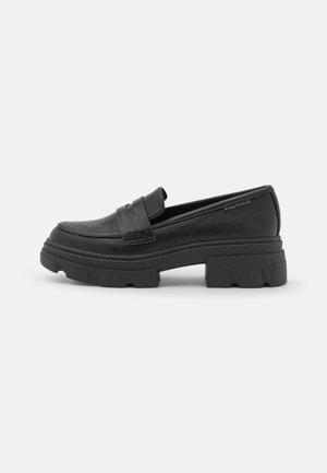 Black chunky loafer with thick lug sole, smooth leather upper, strap detail across the vamp, and subtle brand logo near the heel.