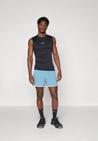 Top desportivo preto sem mangas com logótipo branco, combinado com calções azul claro com acabamento branco. Tênis desportivos pretos e meias completam o conjunto.