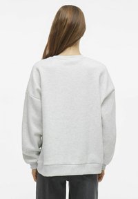 Svetlo siva majica s kapuljačom, spuštenim rameni in rebrastimi zapestji. Mehka tekstura in ohlapen kroj. Zadnji pogled prikazuje minimalne oblikovalske podrobnosti.