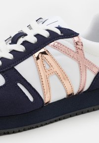 Navy and white sneaker with rose gold 'AX' branding, suede and mesh materials, round laces, and perforated accents on the sides.