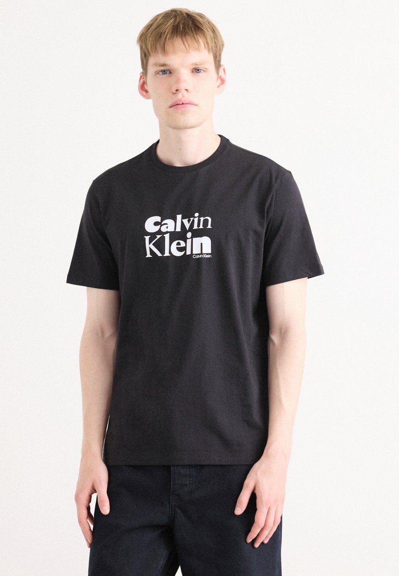 Melna kokvilnas T-krekls ar īsām piedurknēm, kurā ir balts "Calvin Klein" logo. Vienkāršs dizains, apaļa kakla izgriezuma, standarta piegriezums.