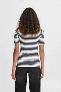Stribet kortærmet top med marineblå og hvid ribbet stof, bølgede kanter og en tætsiddende silhuet, parret med sorte jeans.