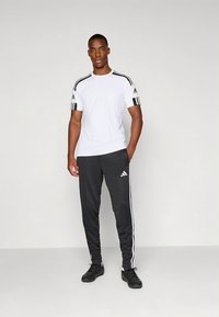 Fehér Adidas sportpóló fekete vállcsíkkal, fekete melegítőnadrággal, melyen fehér oldalsávok és egy kis logó található. Fekete sportcipő.