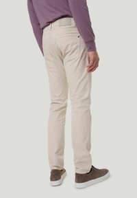 Beige Baumwollhosen im Slim-Fit-Stil, mit vier Taschen und strukturiertem Finish. Getragen mit braunen Sneakers. Von hinten betrachtet.