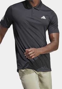 Czarny szary polo z miękką, gładką fakturą. Posiada trzy guziki, krótkie rękawy oraz białe logo na górnej lewej stronie.