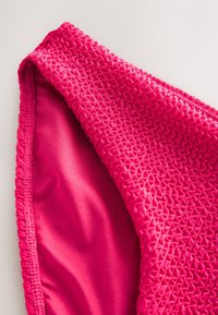 Tissu de maillot de bain fuchsia à surface texturée, avec des détails froncés et une doublure intérieure lisse. Contraste de couleurs net.
