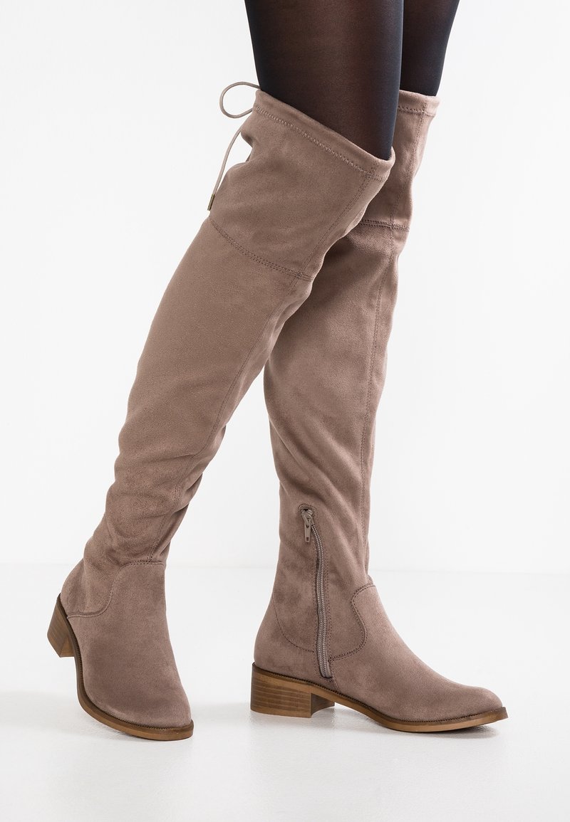 Bottes montantes en daim taupe avec un design décontracté, fermeture éclair latérale et petit talon bloc, présentant une texture lisse et des détails de couture soignés.