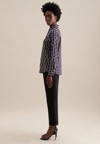 Camicia a maniche lunghe viola a fantasia con un design a catena, abbinata a pantaloni neri su misura e sandali neri con tacco alto.