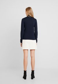 Smal passform i marinblå tröja med långa ärmar och hög krage, tillsammans med en vit denimkjol ovanför knät och svarta klackiga ankelboots.
