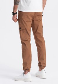 Bruine cargo-broek met zijzakken, elastische boorden en een relaxte pasvorm, gecombineerd met witte sneakers. Soepele stoftextuur.