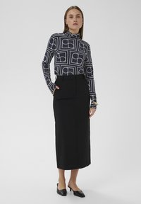 Falda lápiz larga negra combinada con un jersey de cuello alto ajustado que presenta un patrón geométrico blanco. Corte entallado, textura suave y diseño minimalista.