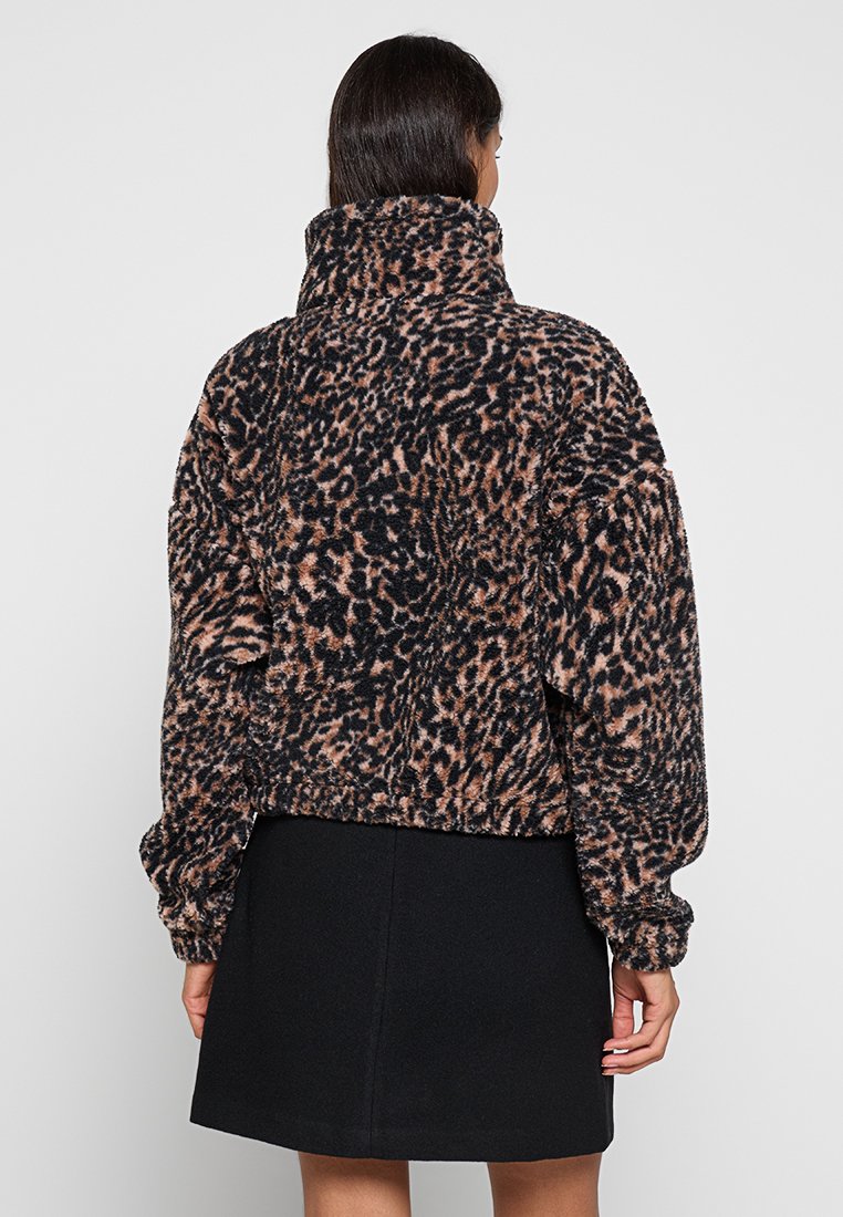 Chaqueta de estampado de leopardo en un tejido suave y esponjoso con un alto cuello. Diseño cortado, mangas largas y dobladillo elástico. Combinada con una falda negra.