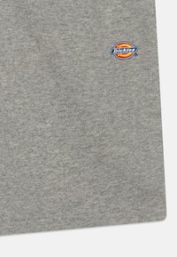 T-shirt en coton gris avec une texture côtelée, arborant un petit logo coloré "Dickies" sur la partie gauche de la poitrine. Design simple à col rond.