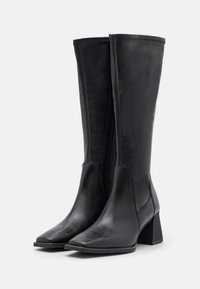 Botas de cuero negras hasta la rodilla con punta afilada y tacón cuadrado. Textura lisa con detalles de costura y una cremallera en el lado.