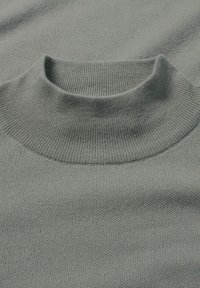 Helles graues Strickoberteil mit hohem, geripptem Kragen und feiner Textur. Der Stoff wirkt weich und gleichmäßig in Farbe und Muster.