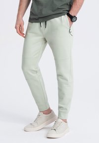 Lichtgroene joggers met een taps toelopende pasvorm, details in de zakken en elastische boorden, gecombineerd met lichtbeige sneakers. Gemaakt van een zachte katoenmix.