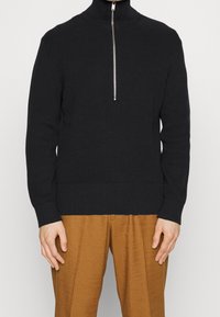 Maglione nero a coste con colletto alto e chiusura con cerniera argentata, caratterizzato da maniche lunghe e punto vita aderente.