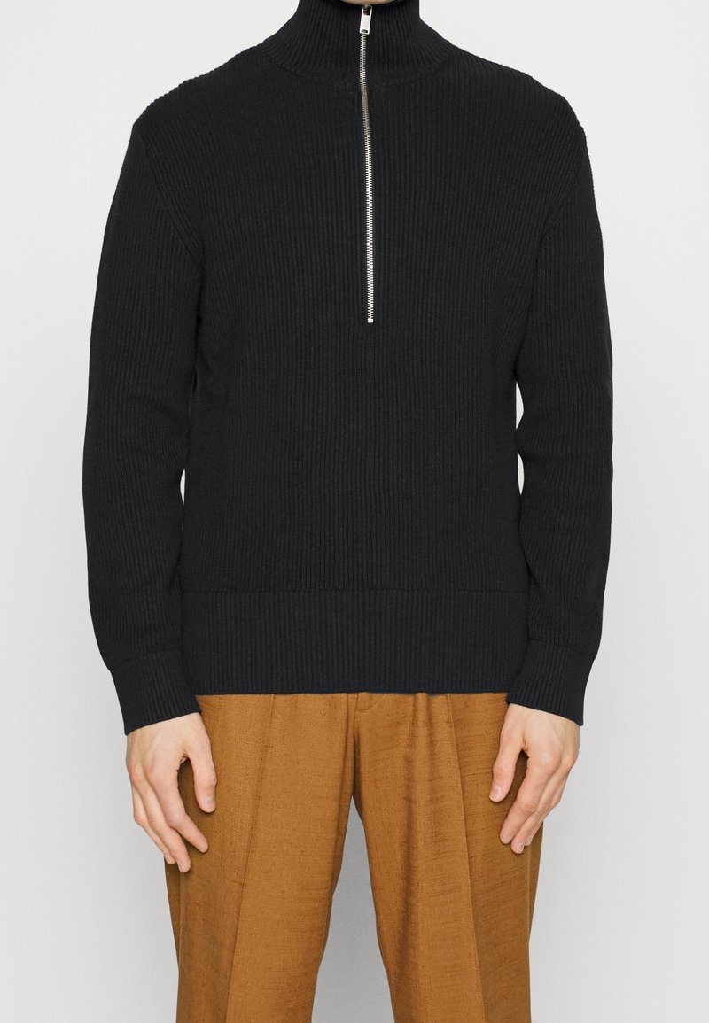 Maglione nero a coste con colletto alto e chiusura con cerniera argentata, caratterizzato da maniche lunghe e punto vita aderente.