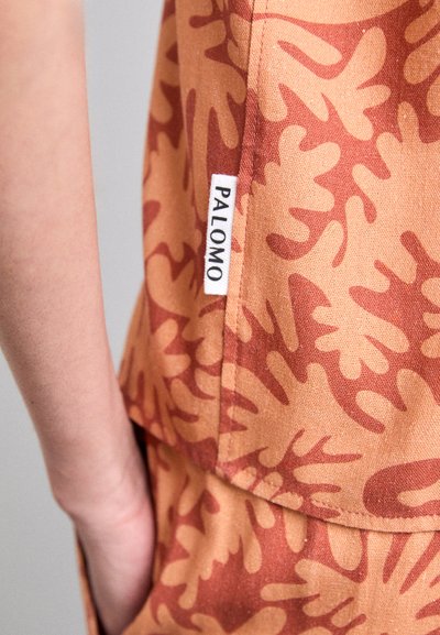 Palomo top in orange-brown fabric features a leaf-patterned design. A label with "PALOMO" is visible on the side seam.