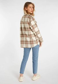 Gecheckte wollen overhemdjack in crème en bruin, met een relaxed fit, knoopmanschappen en zijsplitten, gecombineerd met lichtblauwe jeans en sneakers.