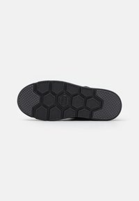 Schwarze Schuhsohle mit einem hexagonalen Muster und strukturierten Bereichen für Grip. Das Design ist flach und aus strapazierfähigem Gummi gefertigt.