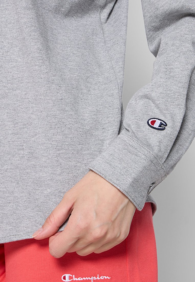 Helles graues Langarmshirt aus Baumwollmix mit geripptem Bündchen und besticktem Logo, kombiniert mit korallenfarbenen Pants.