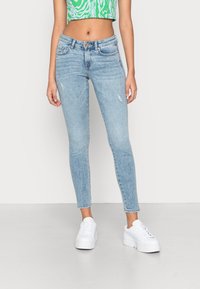 Jeans skinny em azul claro com detalhes desgastados, design de cinco bolsos, bainhas desfiadas e cintura média, combinados com ténis de plataforma brancos.