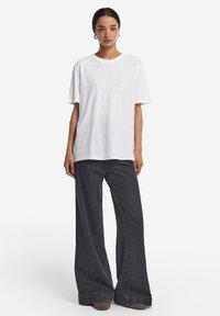 Hvid, kortærmet t-shirt lavet af blødt bomuld, parret med højtaljede, vide, mørk denim jeans og grå fodtøj. Enkel design, ingen mønstre.