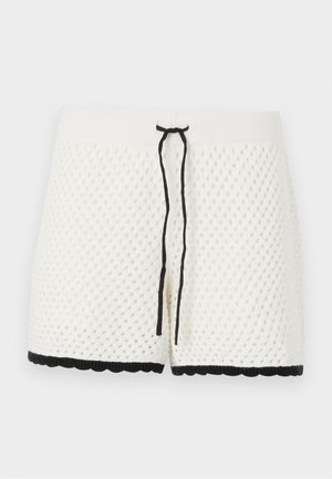 White knitted shorts with a textured, diamond pattern. Features a black drawstring at the waist and scalloped black trim along the bottom.