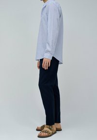 Camicia a maniche lunghe a righe in azzurro chiaro e bianco, abbinata a pantaloni navy e sandali marroni, caratterizzata da un taglio rilassato e collo standard.