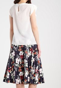 Blusa blanca de manga corta con un detalle en forma de ojal en la espalda, combinada con una falda de tablas azul marino con un colorido estampado floral.