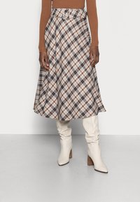 Karierte Midi-Rock mit gegürteter Taille in Braun, Creme und Blau. Getragen mit kniehohen, cremefarbenen Schaftstiefeln und einem taillierten Oberteil.
