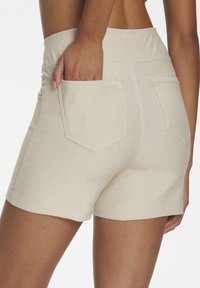 Light beige shorts with two back pockets, worn by a person with one hand placed inside the left pocket.
