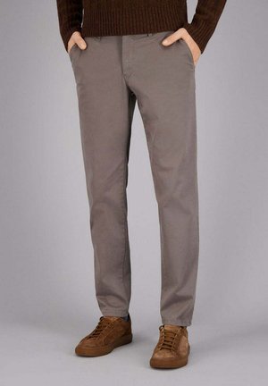 Beige Baumwoll-Chinos mit geradem Bein und seitlichen Taschen, kombiniert mit braunen Wildleder-Sneakern, auf einem neutralen Hintergrund.