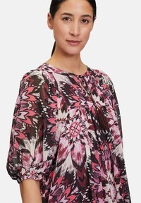 Blusa a fantasia in tessuto leggero, con audaci design floreali in rosa, nero e bianco, scollatura rotonda e dettaglio con nappina.