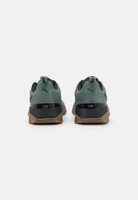 Zapatillas de malla verdes con acentos negros, punta redonda y suela de goma marrón. Cuenta con un asa y un detalle del logo en el talón.