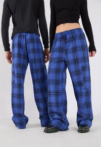 Blå rutiga byxor med svarta accenter, bred ben-design, elastisk midjeband och sidofickor. Bärs med åtsittande toppar och kraftiga skor.
