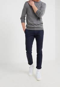 Grå bomullströja med långa ärmar, kombinerad med marinblå avsmalnande byxor och vita sneakers. Outfiten har en avslappnad och ledig design.