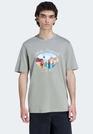 Camiseta de manga corta gris claro, con un colorido estampado gráfico en forma ovalada, con el texto "Adidas Originals" y "Berlín" debajo.