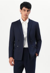 Sacou bleumarin cu două rânduri de butoni, dintr-un material texturat, având rever în formă de fason și două buzunare frontale, asortat cu o cămașă albă.