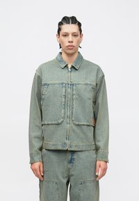 Τζιν μπουφάν σε ανοιχτό μπλε, με φερμουάρ μπροστά, δύο μεγάλες τσέπες και γιακά. Φθαρμένη υφή με ορατές ραφές.