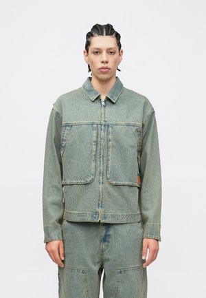 Hele sinine teksajope, millel on ees tõmblukk, kaks suurt taskut ja kraega kaelus. Kulunud tekstuur koos nähtavate õmblustega.