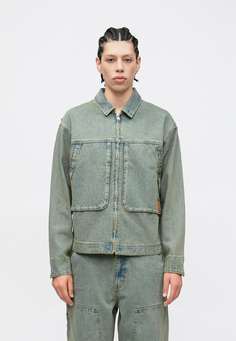 Τζιν μπουφάν σε ανοιχτό μπλε, με φερμουάρ μπροστά, δύο μεγάλες τσέπες και γιακά. Φθαρμένη υφή με ορατές ραφές.