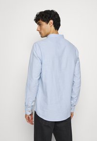 Lyseblå langermet skjorte laget av et teksturert stoff, med standard krage og knappede mansjetter, og buet kant.