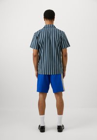 Trumpai rankovėmis marškiniai su vertikaliomis mėlynomis ir baltomis juostelėmis, derinami su ryškiai mėlynomis šortais, turinčiais šonines juosteles. Juodi batai ir balti kojinės.