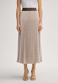 Mulher vestindo uma saia midi plissada bege com um design estampado e uma faixa escura na cintura, combinada com uma blusa branca e sapatos de salto com tiras no tornozelo bege.