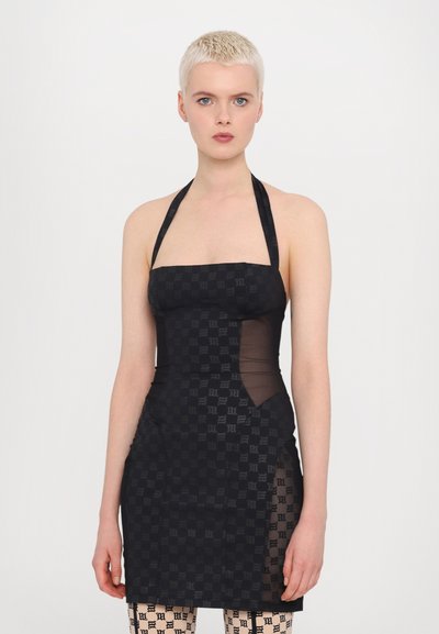 Rochie neagră cu guler halter, cu un model în carouri, panouri laterale transparente și o siluetă ajustată. Model care poartă ciorapi negri transparenți cu model.
