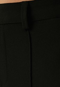 Lähenemine mustale kangale õmblusega ja vöösilmaga rõival, näidates tekstuuri ja õmblusdetailsusi.